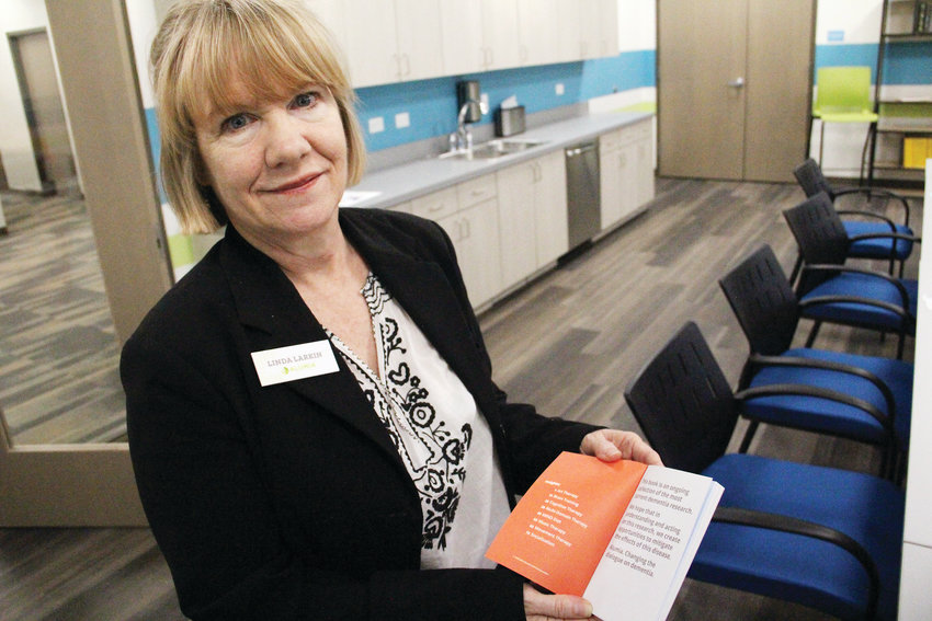 Linda Larkin, art therapist at Alumia Institute, holds up on Dec. 18 a book of easy-to-read advice and insights — based on research — for people or families who have received a dementia diagnosis. Alumia is a therapy campus for those in the early stages of dementia, located at 9800 E. Geddes Ave.