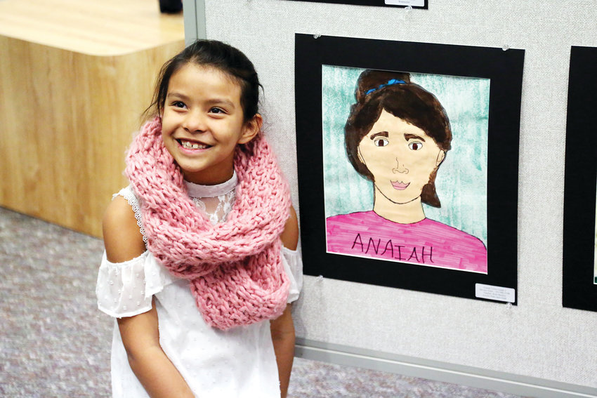Anaiah Cortes, student at Stevens Elementary, poses for a picture next to her self-portrait.