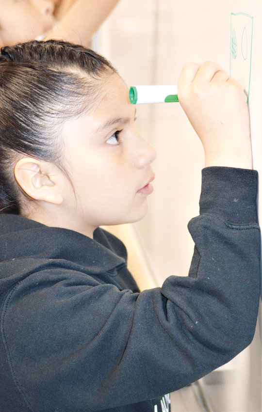 Valentina Quinones, a second grade student at Thornton’s STEM Launch School, draws a robot on a whiteboard at Amazon’s Thornton warehouse.