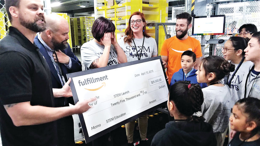 Clint Autrey, left, general manager of Amazon's Thornton warehouse, presents a $25,000 check to Adams 12's STEM Launch School Principal Martin McCarthy and Maker Lab coordinator and technology teacher Deborah Harding, second and third from left, April 10. The Amazon warehouse opened its doors to a group of STEM Launch students, letting them show off their skills and tour the robotically-controlled facility.