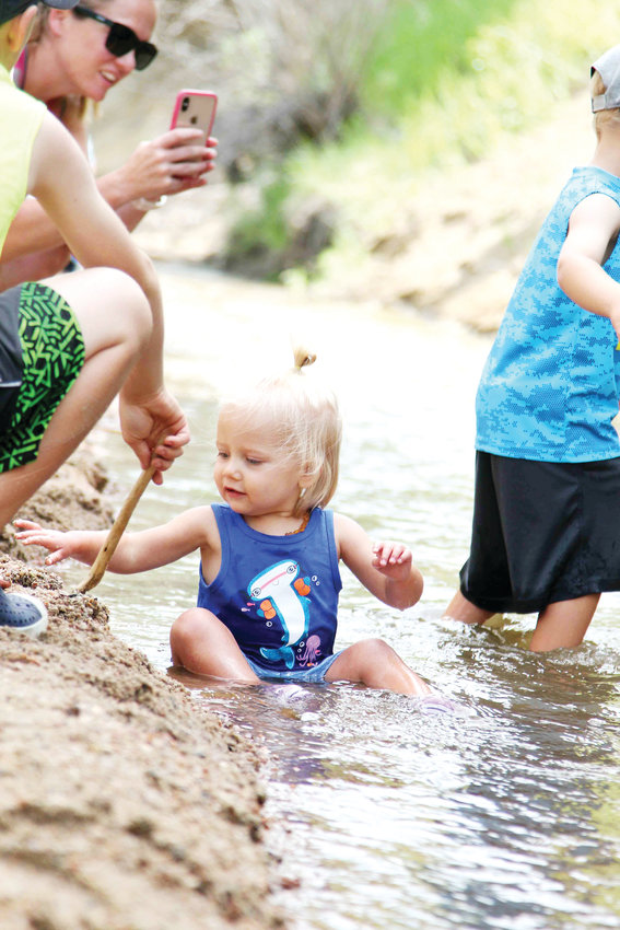 Kaitlee Dwitley sits in the creek while her mother, Heather, takes a photo and siblings play nearby during the annual Ducky Derby in Castle Rock.