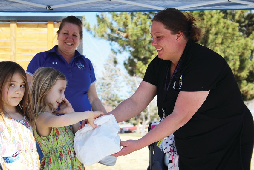 Kahlesi Johnson, left, and Rose Johnson receive food at Cherrelyn Elementary from Kendra Schappaugh, kitchen manager at Colorado's Finest High School of Choice. Englewood Schools has been providing free food to students at sites at Cherrelyn Elementary and Bishop Elementary.