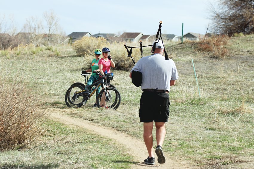 Mountain bikers Jenn Cummings and Susan Davis pulled over to the side of a trail in Dad Clark Park to take photos as Andrew Michaud passed by playing his bagpipe April 1.