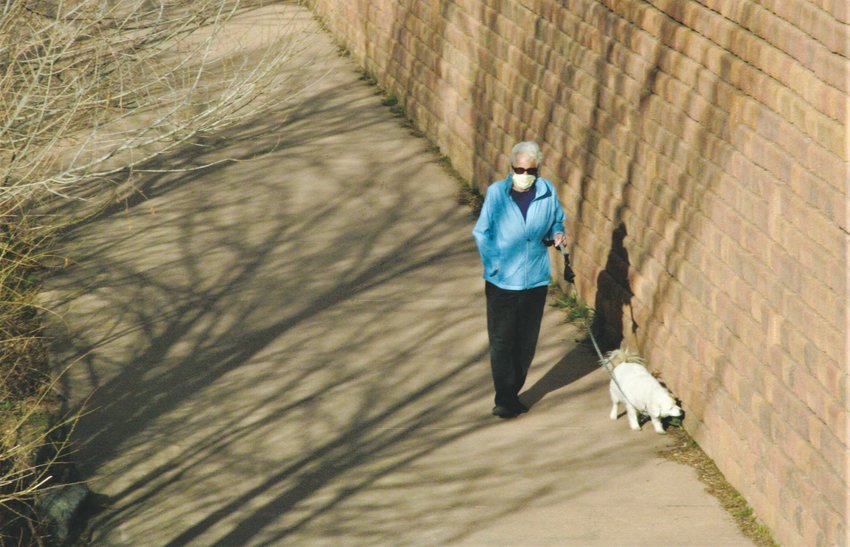 A woman wears a mask while she walks her dog along the Clear Creek trail in Golden.