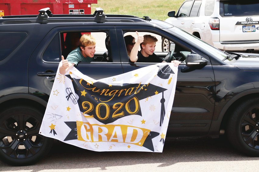 Two boys give thumbs-up after a ThunderRidge High School teacher shouts “be good” as they pass by during a May 15 parade of graduates.