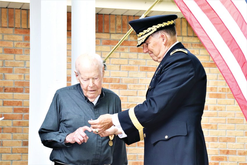 Retired Major General Steven Best holds up a medal for Reverend Edward Flaherty, Jr. to see before pinning it on him.