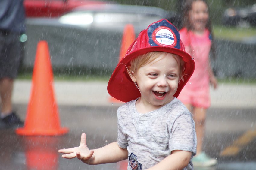 Dillon Goetz, 2, dances beneath a fire hose’s spray.