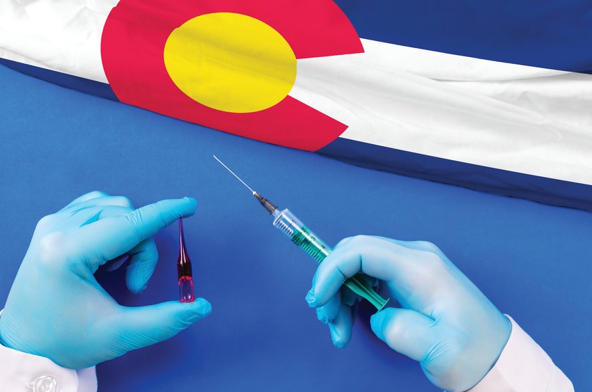 Colorado Vaccination. Hands of doctor holding syringe and coronavirus (COVID-19) vial vaccine on flag Colorado