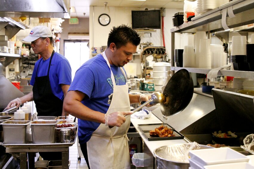 Chef Jose Lara, center, plates an order of sesame chicken while chef Xie Zhi, left, prepares sweet and sour chicken in the kitchen of Honey Pig Cafe on Sept. 6.