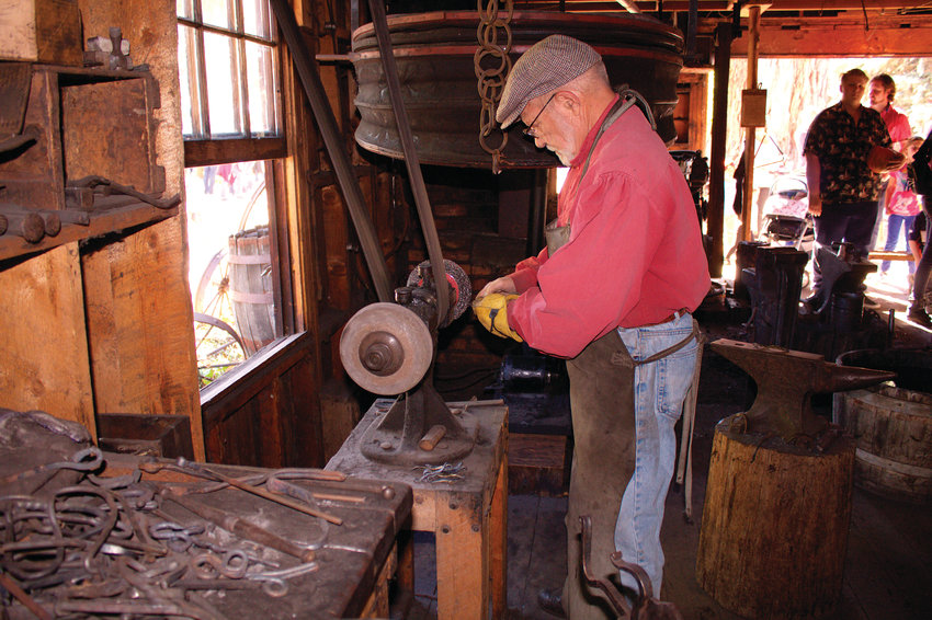 The blacksmith at Littleton Museum, explaining the process, works on a project while families stand nearby and watch during the Oct. 13 Harvest Festival.