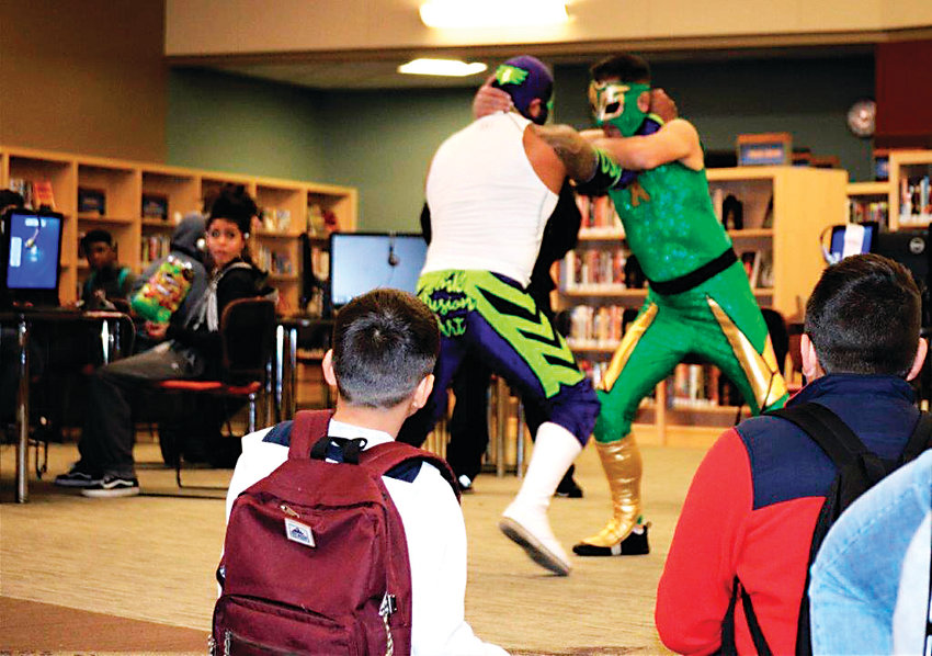 Professional wrestlers, or luchadores, Heros, in white, and Sol Azteca, square off in the middle of Anythink Library’s York St. branch Feb. 26. Anythink Guide Michelle Hawkins invited the pair to the library to show off some of their moves and talk to the patrons about what Mexican wrestling means to them.