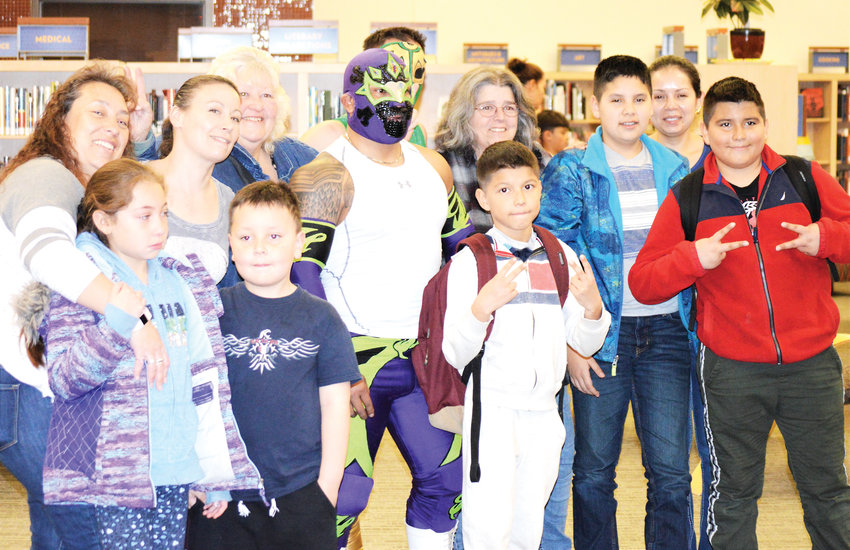 Mexican wrestlers Heros, in white, and Sol Azteca in green pose with Anythink Library patrons and staff Feb. 26 after presenting a demonstration of their craft and talking about it.