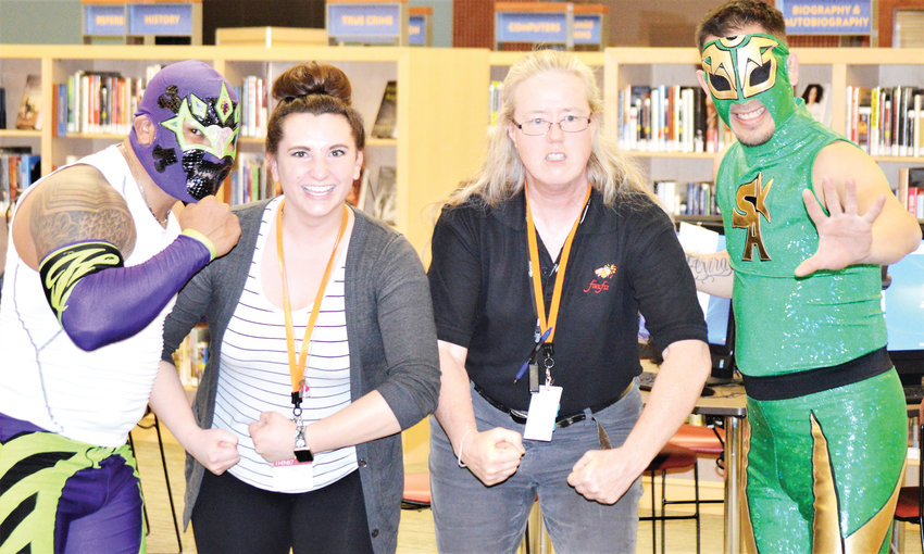 Anythink Library York Street concierges Gina Collette, left, and Heather McCuistion pose with luchadores Heros and Sol Azteca Feb. 26. The pair of Mexican wrestlers both work in Denver through Lucha Libre Life and showed off their moves at the library.