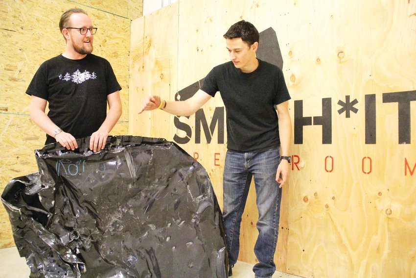 Drew Neilson holds a busted-up car hood while Dustin Gagne points to damage Sept. 24 at their business, Smash It Breakroom. Called a rage room or smash room, it bills itself as fun, safe stress relief.
