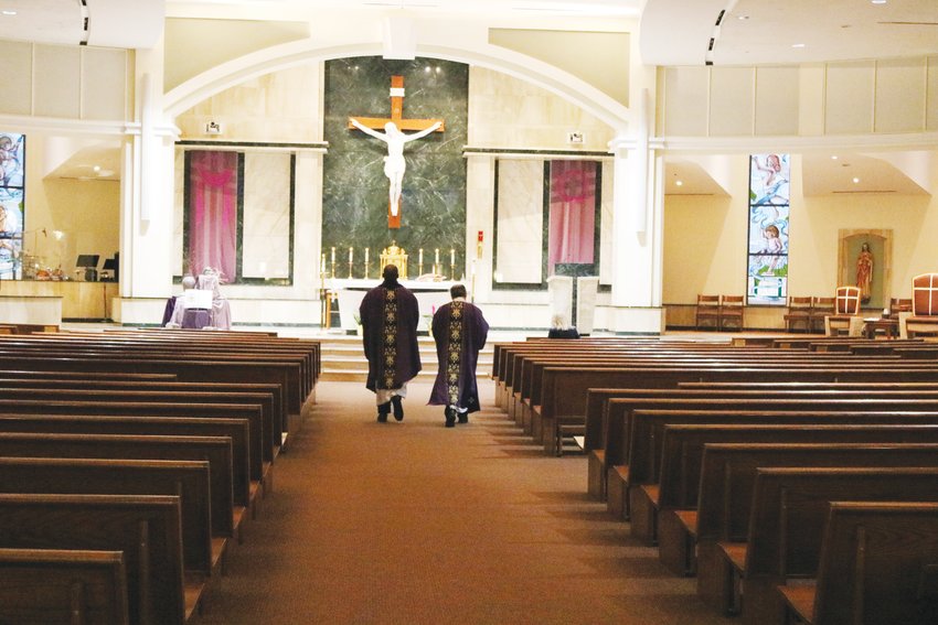 Father John Judanha and Deacon George Morin walk down the aisle at St. Thomas More Catholic Church in Centennial before beginning their livestreamed service. The church was nearly empty except for a few staff members and the church's AV team.