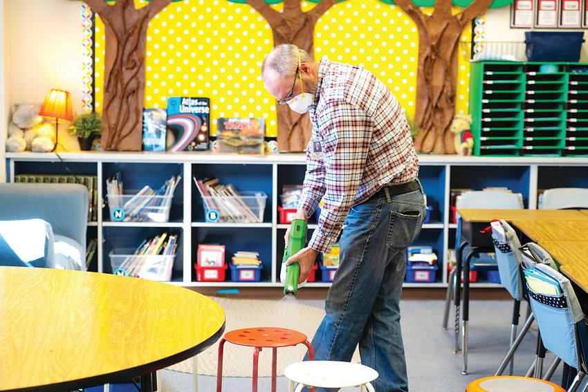A man sprays a seat for young children during cleaning procedures in Cherry Creek School District as a precaution against COVID-19.
