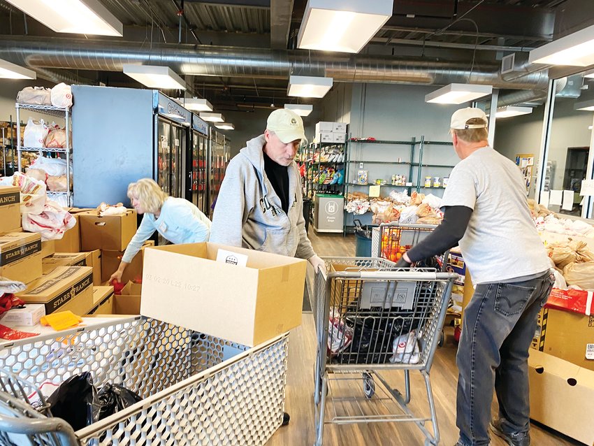 Volunteers pack bags of food items, about enough to feed a family of four for a week, into shopping carts to be wheeled out to people waiting in their cars.