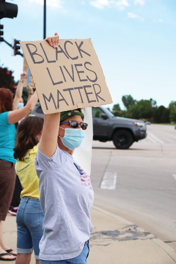 A masked Highlands Ranch resident looks out at traffic on Lucent Boulevard as she holds a Black Lives Matter sign over her head June 8.