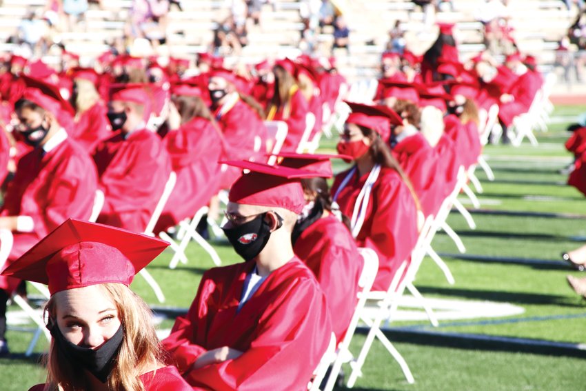 A student, bottom left, engages in an animated conversation with a classmate next to her at Eaglecrest’s graduation ceremony. The students sat in rows spaced apart to comply with social distancing guidelines amid the coronavirus pandemic.