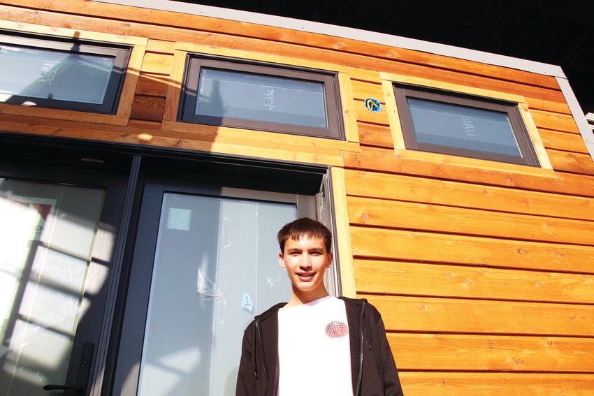 Andrew Dinsdale, an Eaglecrest High School senior, stands in front of one of the tiny homes his class helped create.