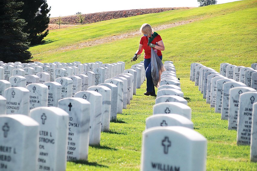 Kathryn McEntire picks up leaves and trash amid the headstones at Fort Logan National Cemetery.