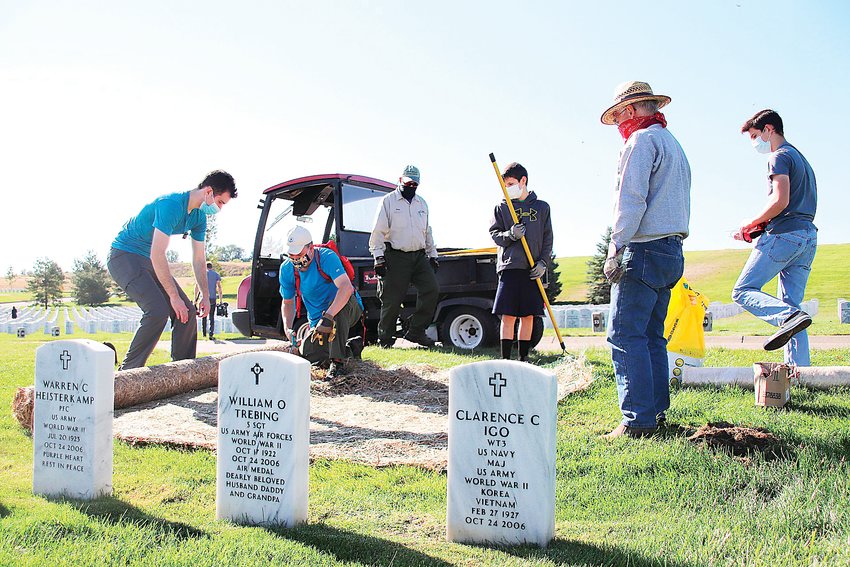 Volunteers unroll landscape matting over a bare spot on the lawn of Fort Logan National Cemetery.