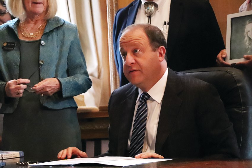 Gov. Jared Polis sits at his desk June 7 in the state Capitol building to sign a bill aimed at addressing bullying policy among school districts in the state.