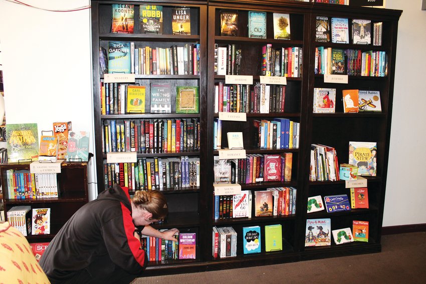 Dyllan Smith, general manager, arranges books on display at One Door Down June 17. The bookstore also features cocktails, smoothies and coffee, and is open 7 a.m.-6 p.m. every day.