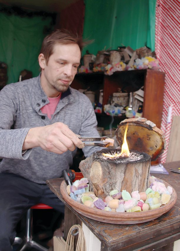 Erik Swanson, owner and founder of The Log Candle, places a piece of wax to feed the candle’s flame. This is Swanson’s first year participating in the Cherry Creek Holiday Market, but he has been selling his product at various other arts-and-crafts markets in the Denver area after launching his company in November 2020.