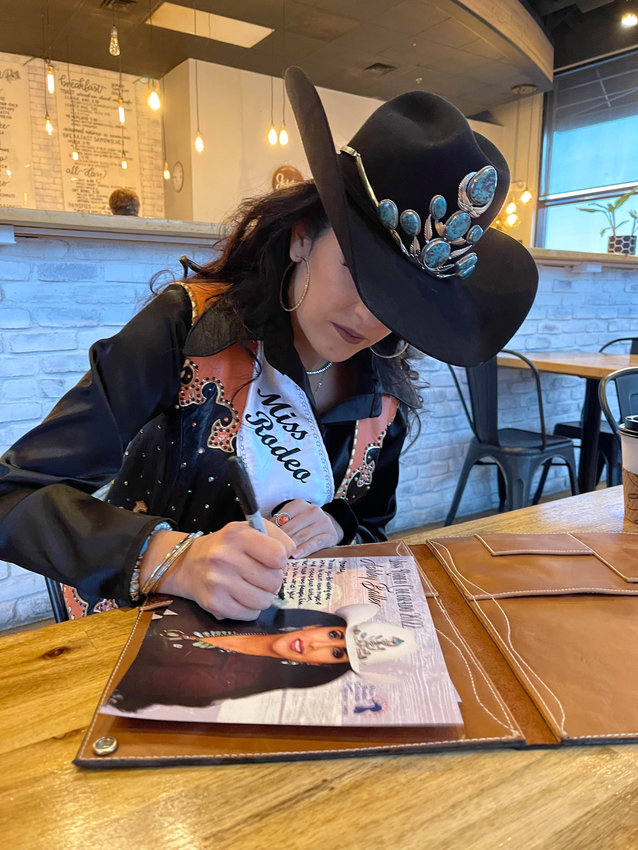 Miss Rodeo Colorado Ashley Baller fills out a signing card, photo pages that rodeo royalty sign and give to people at the National Western Stock Show.