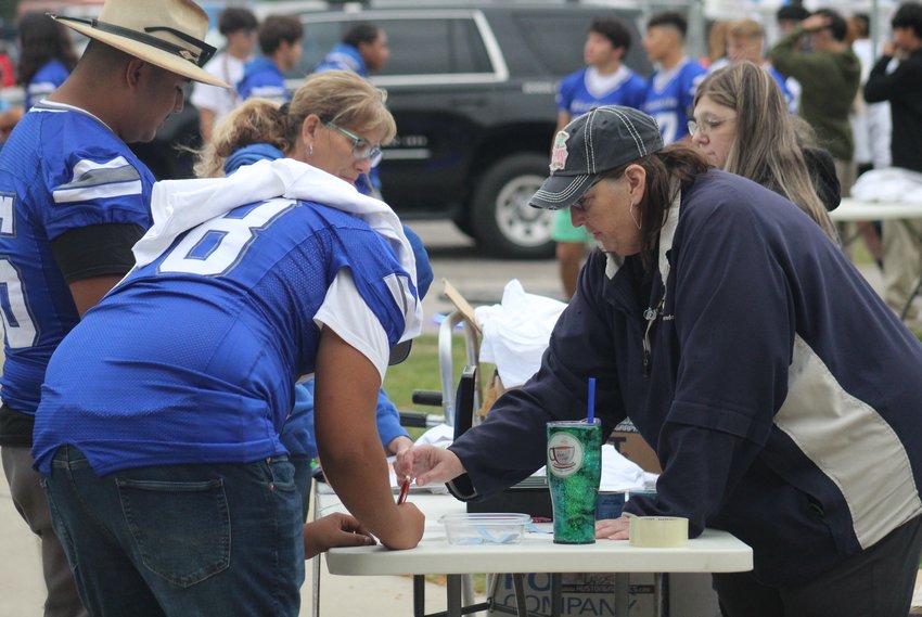 Mary Ellen LeBlanc helps Fort Lupton football player Jovonni Carleton sign in for the Fort Lupton High School Booster Club's barbecue supper and raffle before the Bluedevils' homecoming game Sept. 9. In the background is Weld Re-8 school board President Susan Browne, left, and Michelle Bettger, right.