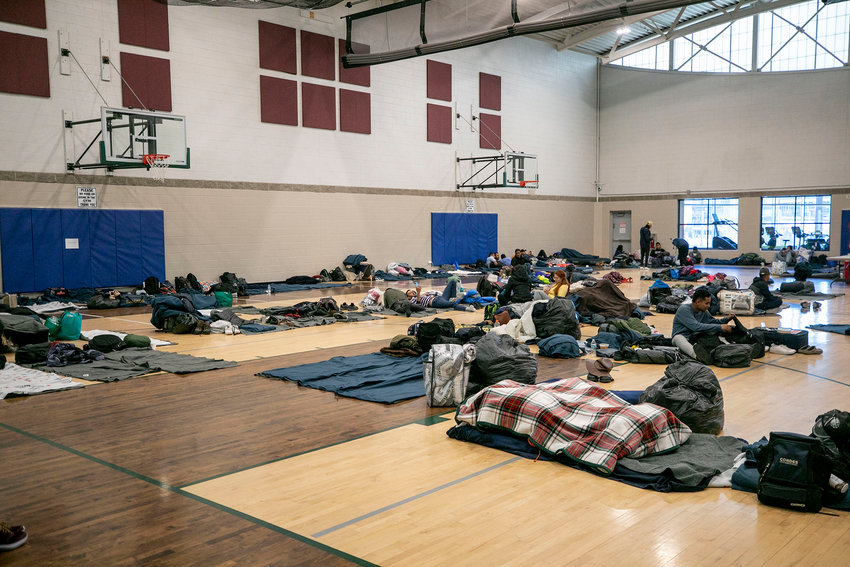 People who’ve arrived from the U.S. southern border hang out on bedrolls on the floor of a Denver rec center, the city’s second emergency shelter. People were originally given cots, but a city spokesperson said they switched to mats to squeeze more people in when they neared capacity in late December.